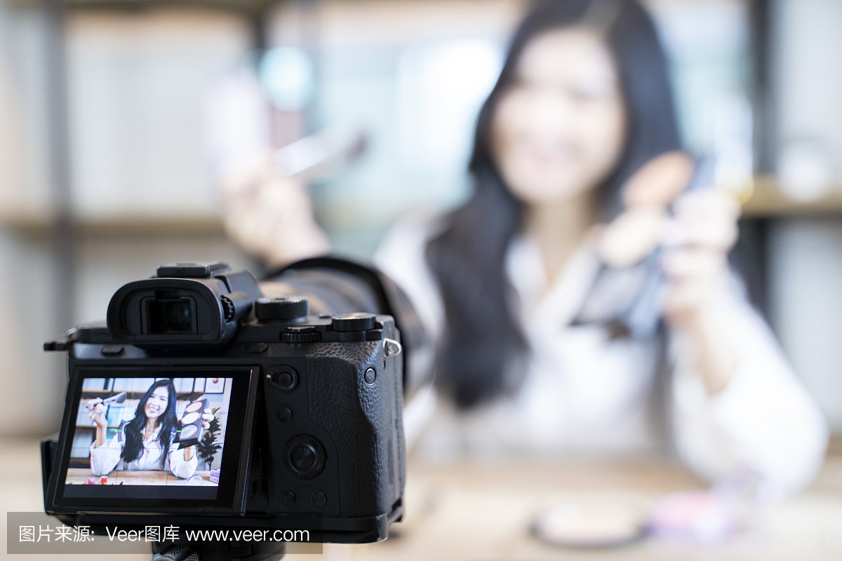 一位亚洲女性博主正在展示如何化妆和使用化妆品。在摄像机前录制在家的视频直播。商业在线影响者对社交媒体的概念。——图片